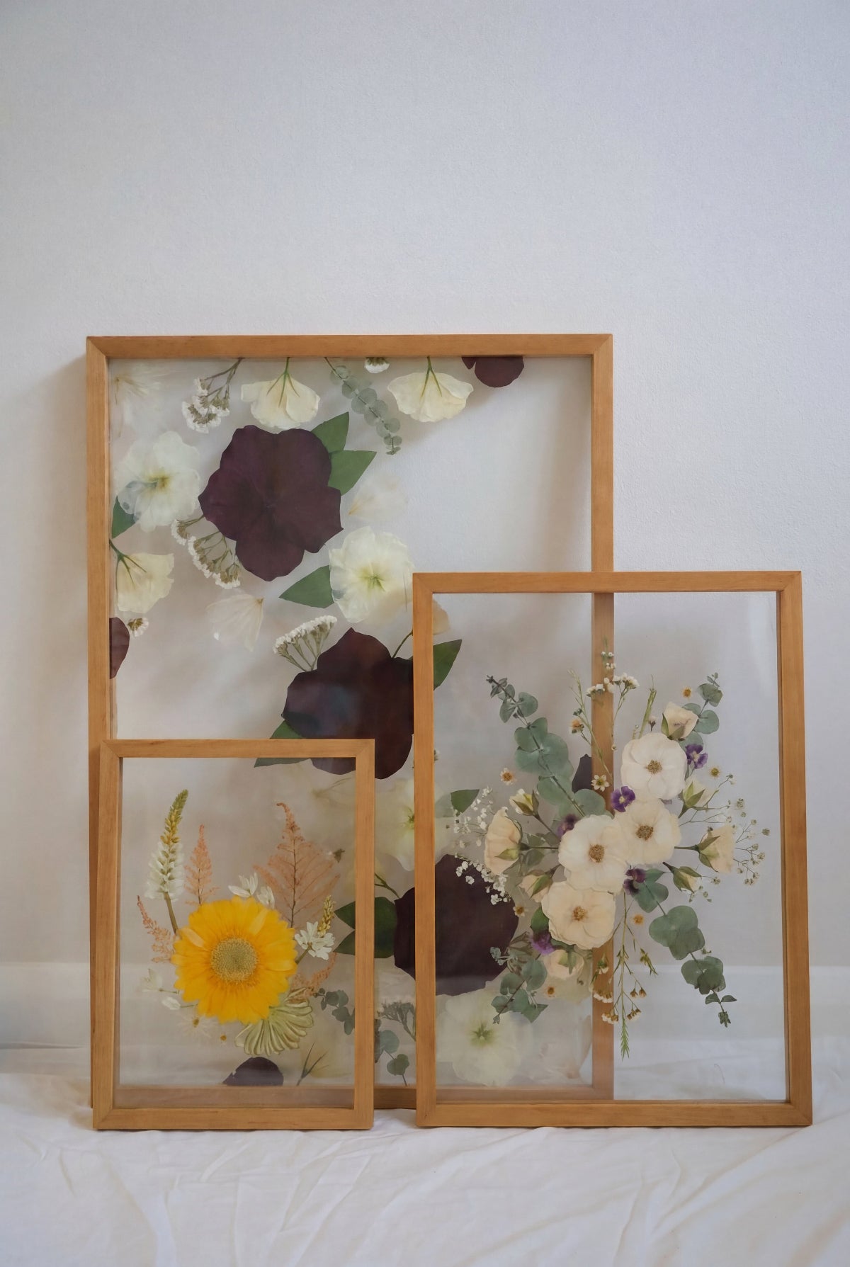 Set of three wooden frames in sizes A2, A3 and A4 with pressed flowers on a white surface.