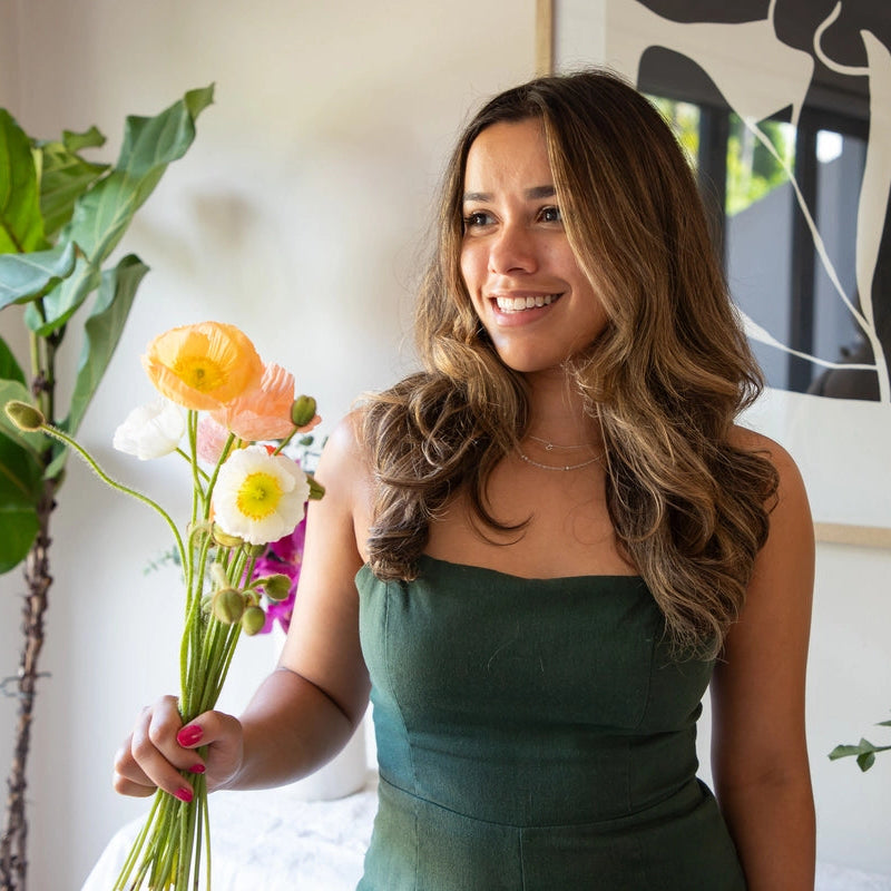 Woman holding flowers indoors with a plant and abstract art in the background
