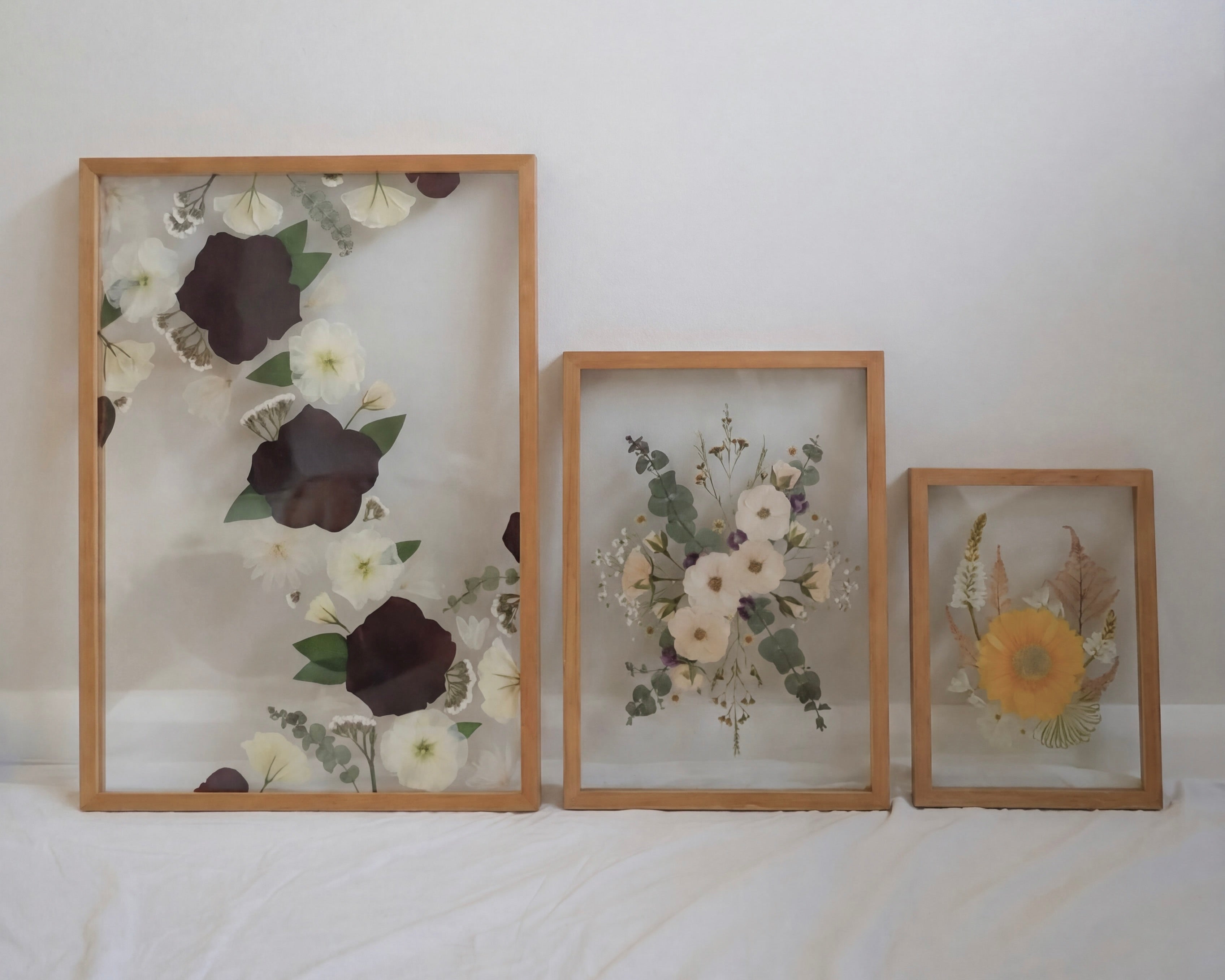 Three framed pressed flower artworks, in sizes A2, A3 and A4 on a white surface with a white background