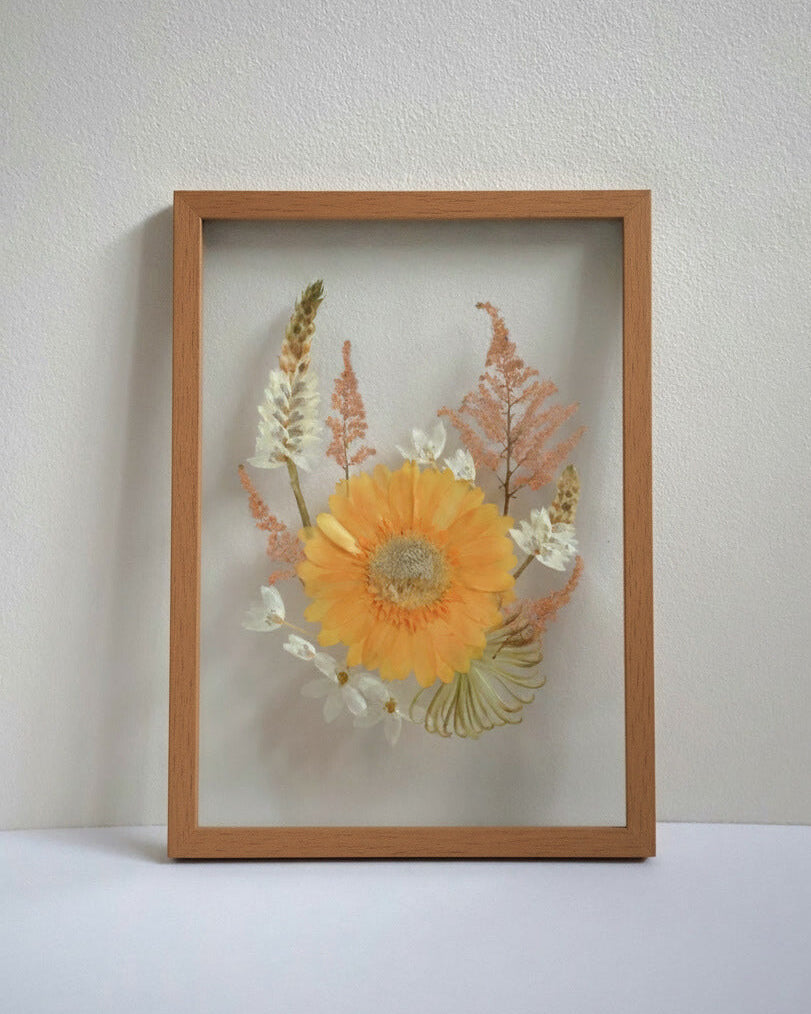 A4 sized framed pressed flowers with a yellow center and green leaves on a white background