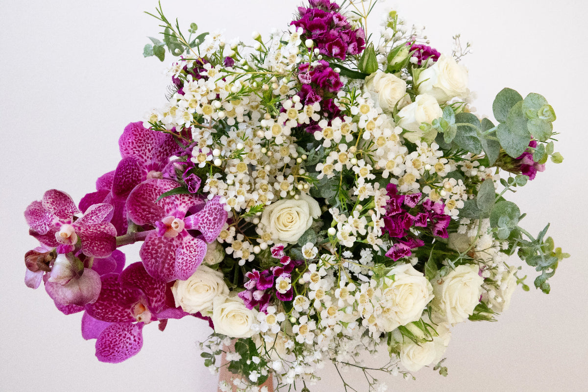 Bouquet of flowers with purple orchids and white roses on a light background